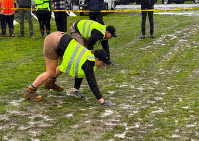 Two Hortisports competitors are in a runner's crouch in the middle of a muddy paddock during a challenge.